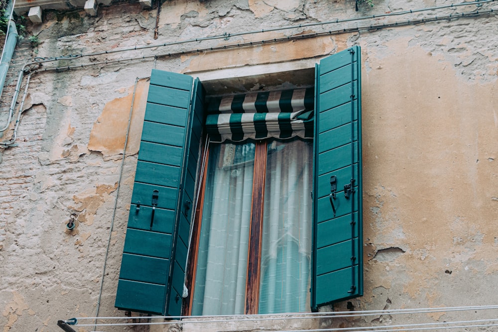 a window with green shutters and a curtain