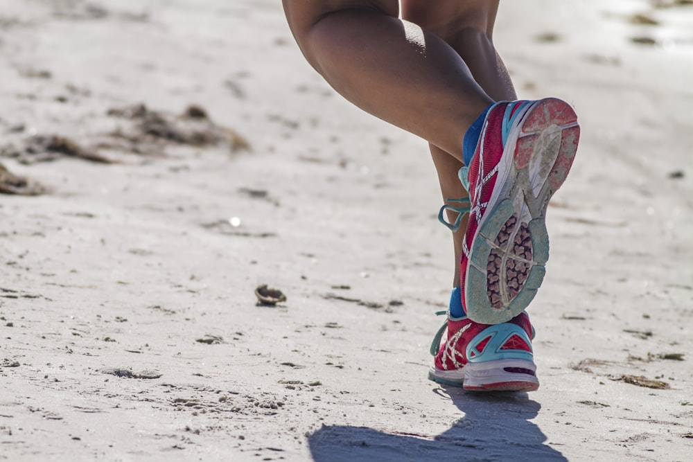 woman in white red and blue sneakers sitting on white sand during daytime