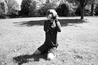 A candid shot of a photographer kneeling to capture a smiling child playing with a pet in a sunlit park.