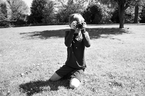 A candid shot of a photographer kneeling to capture a smiling child playing with a pet in a sunlit park.