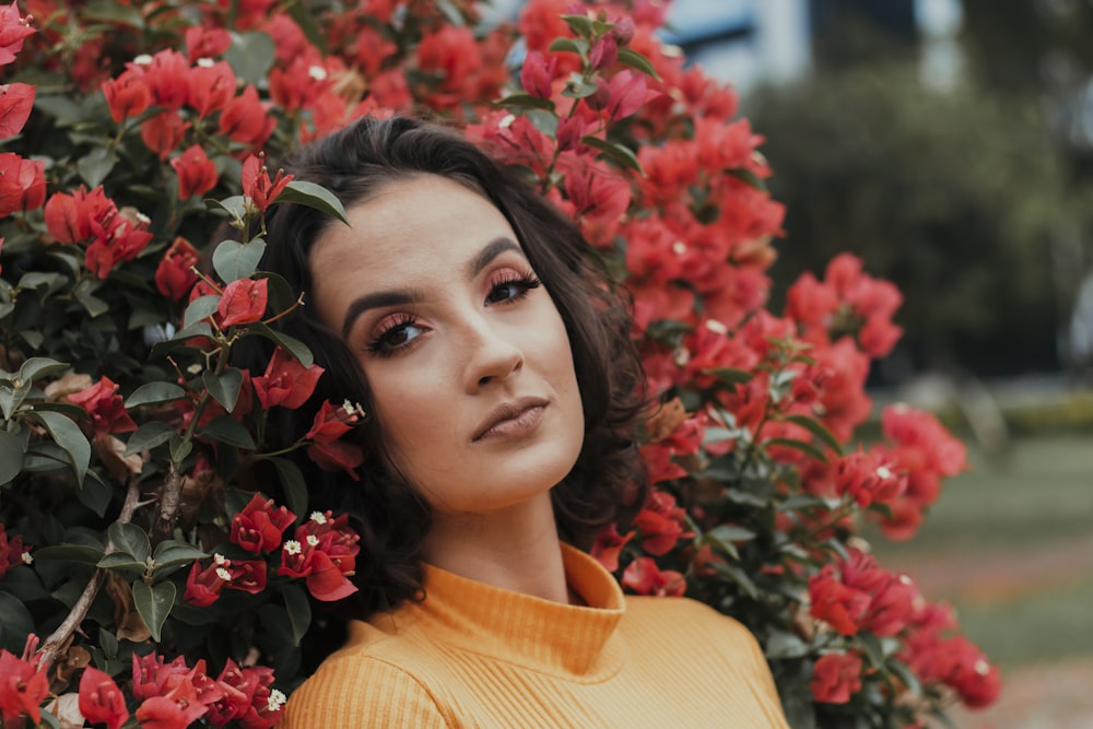 woman in yellow turtleneck shirt standing beside red flowers