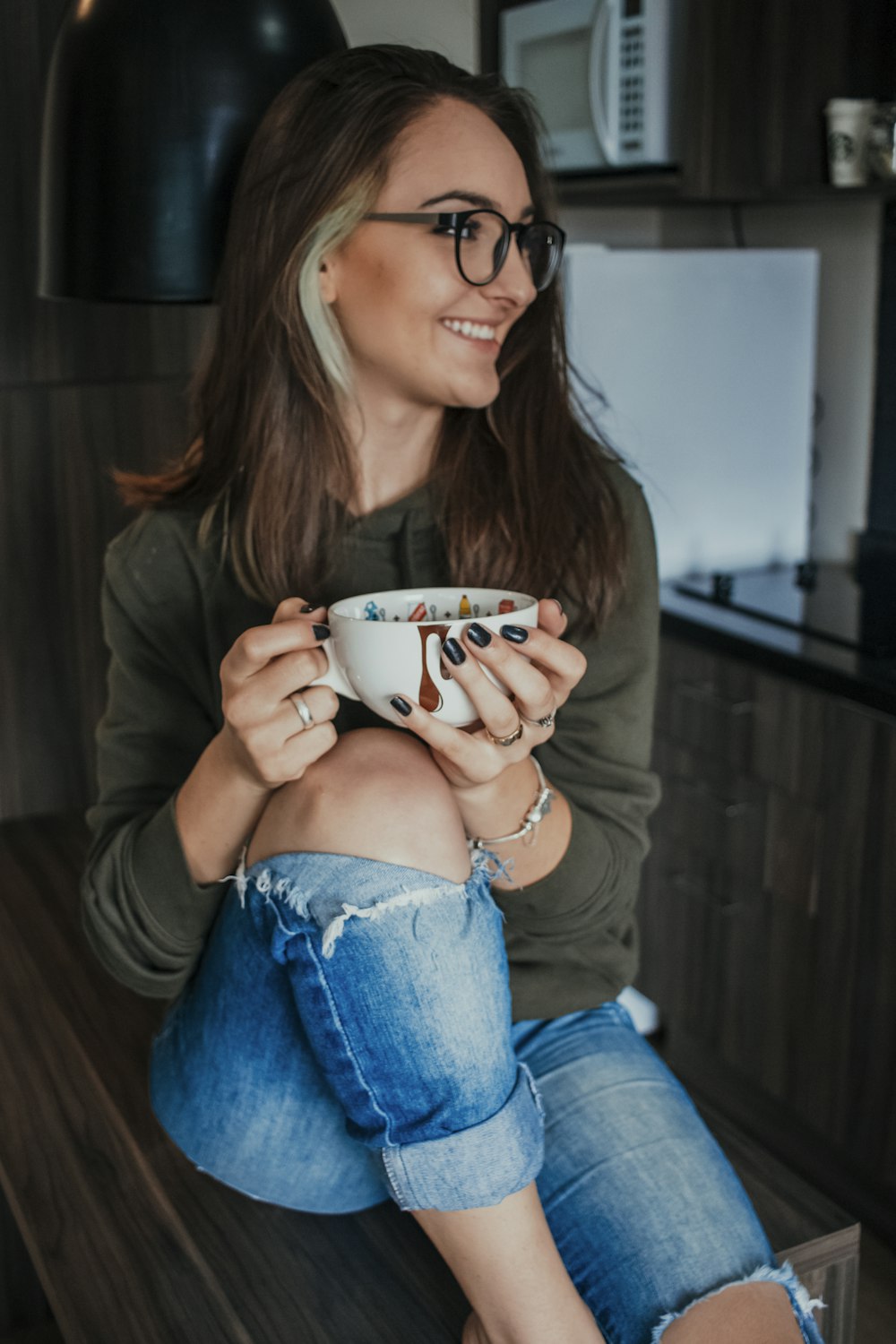 woman in brown long sleeve shirt and blue denim jeans holding white ceramic mug