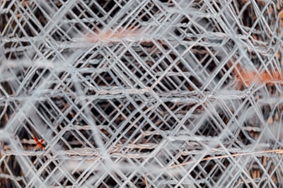 A complex pattern of interwoven metal wires creating a mesh-like structure, with a focus on the intricate crisscross and layering of the wires. The metal has a slightly worn, industrial appearance.