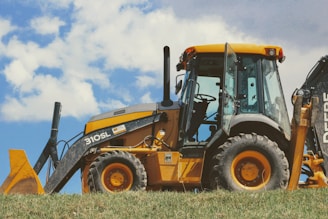 yellow and black front loader on green grass field under white clouds during daytime