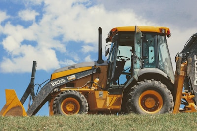 yellow and black front loader on green grass field under white clouds during daytime