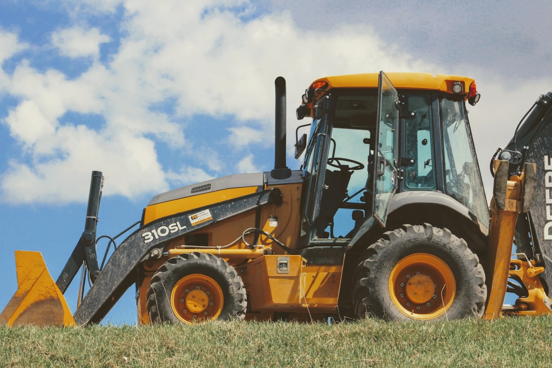 yellow and black front loader on green grass field under white clouds during daytime
