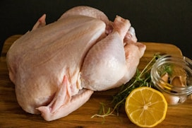 A visually appealing display of fresh chicken cuts on a wooden board, surrounded by herbs and lemon slices.
