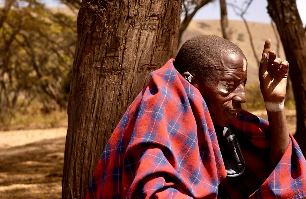 man in red and blue plaid dress shirt sitting beside brown tree