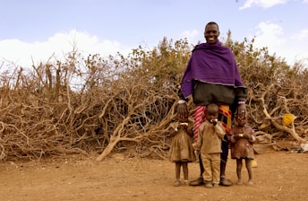 man in purple hoodie standing beside brown bare tree during daytime