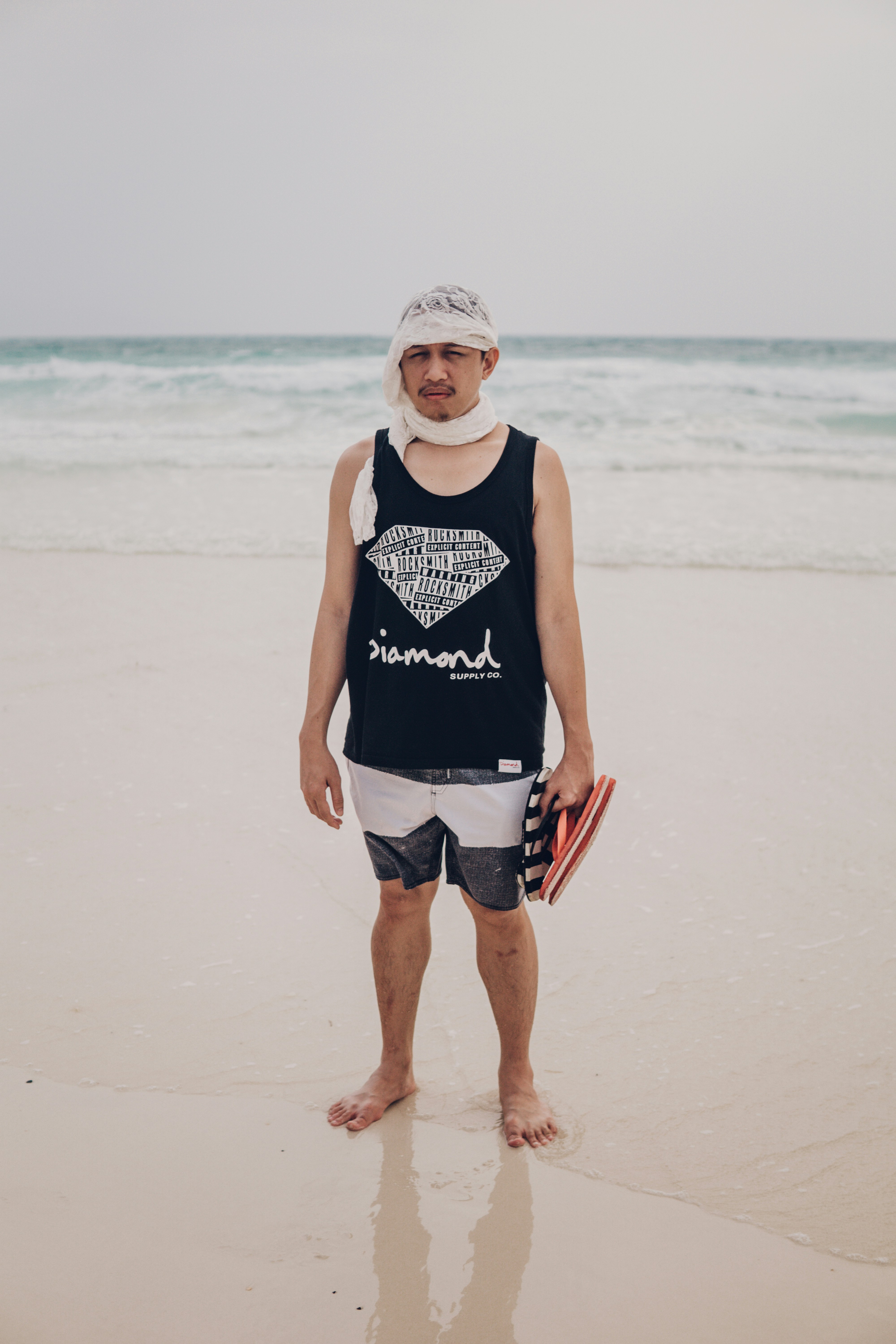 Man in blue tank top and white shorts standing on beach during daytime