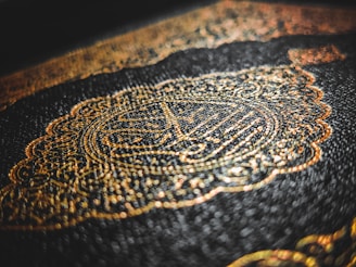 Intricate golden Arabic calligraphy adorns an embossed dark cover, with a rich texture that highlights the detailed craftsmanship.