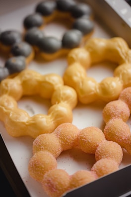 A selection of colorful, round ring-shaped pastries with a distinctive Japanese mochi-style texture featuring different shades. The pastries are arranged in an open box, showcasing their unique appearance.
