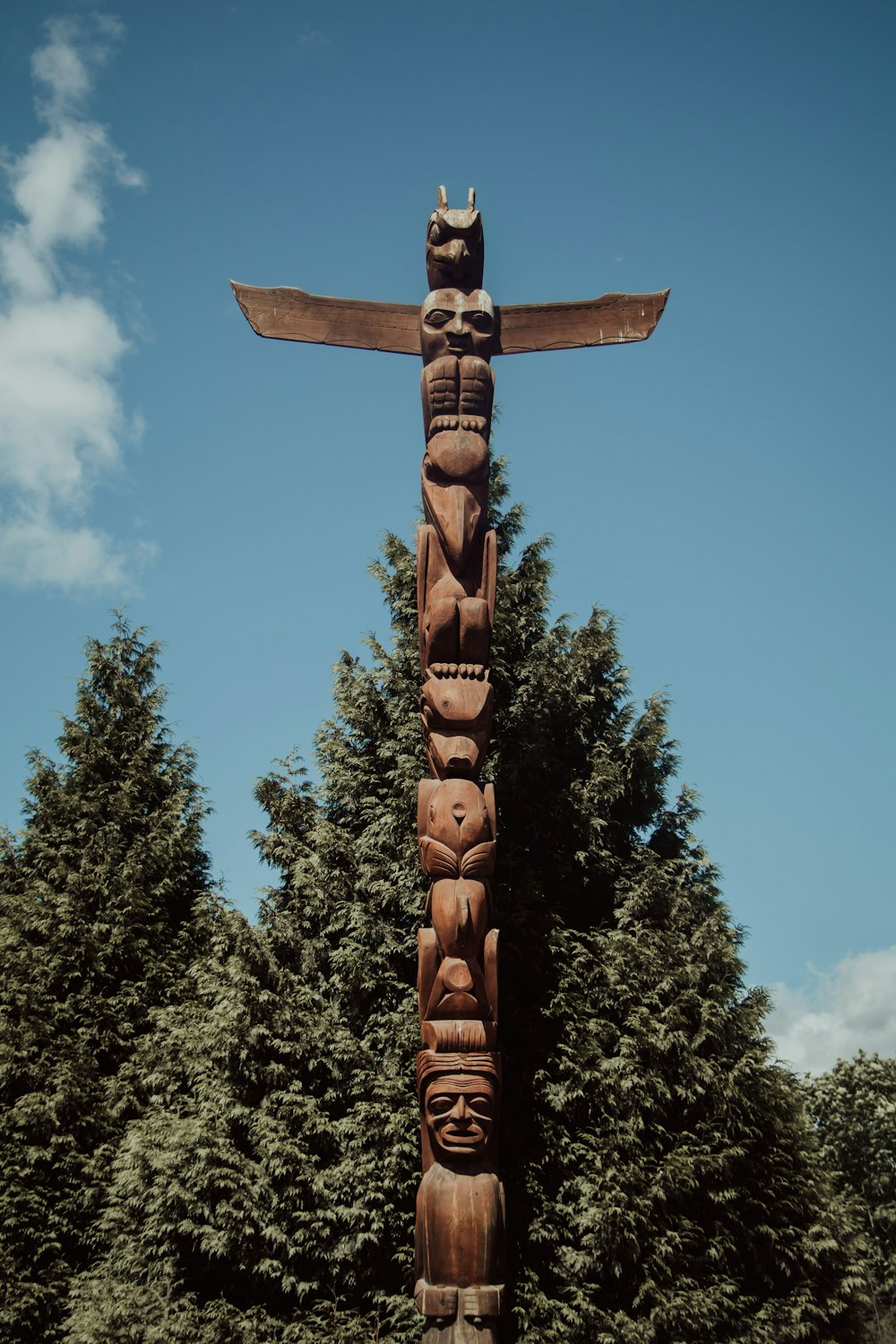 Cruz de madera marrón con hojas verdes bajo el cielo azul durante el día