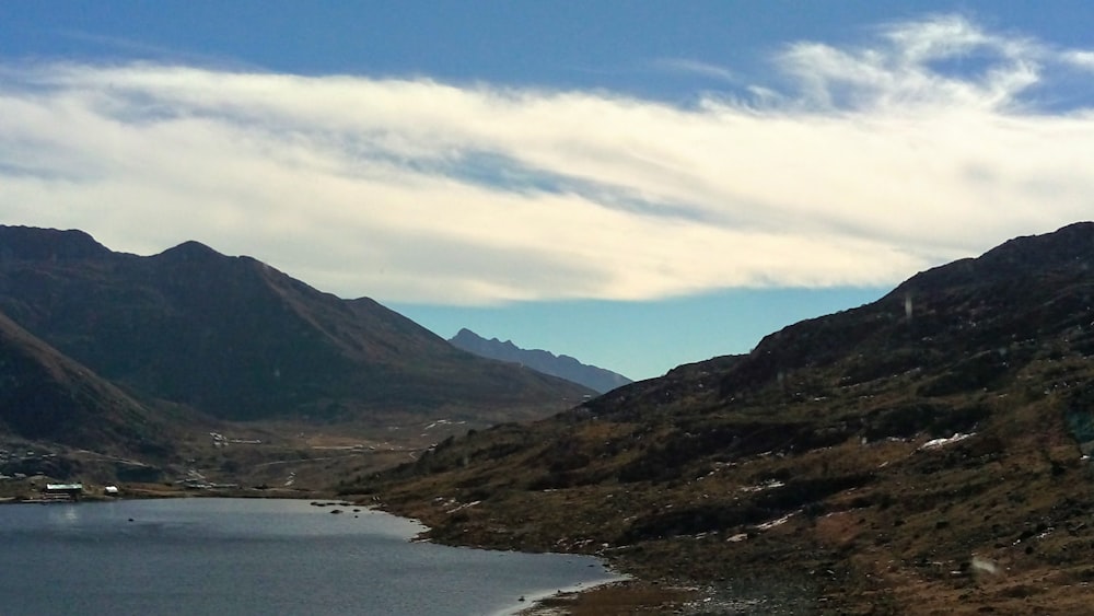 green and brown mountains beside body of water under blue sky during daytime