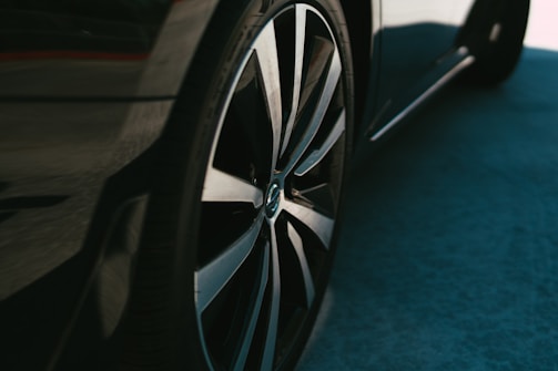 A close-up view of a car tire with sleek, modern alloy wheels. The polished metal reflects light, creating a dynamic and smooth appearance. The vehicle is partially visible with a focus on the wheel and rim.