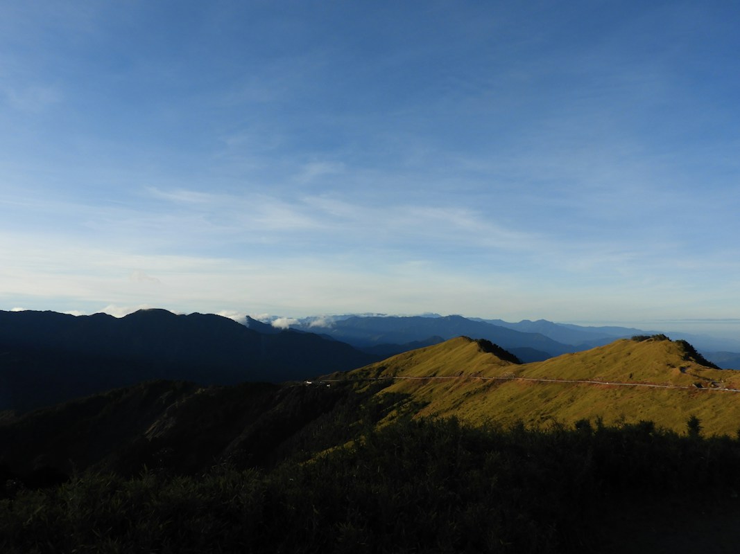 Grassy alpine slopes with layers of mountains in the distance