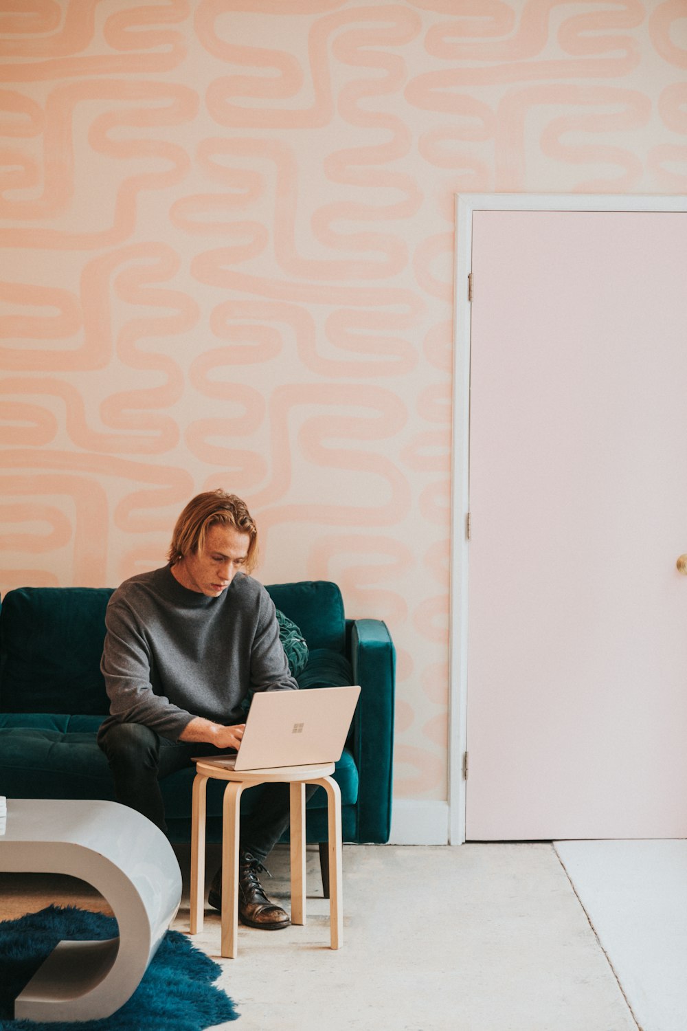 man in gray long sleeve shirt sitting on blue sofa working on a Microsoft Surface laptop 