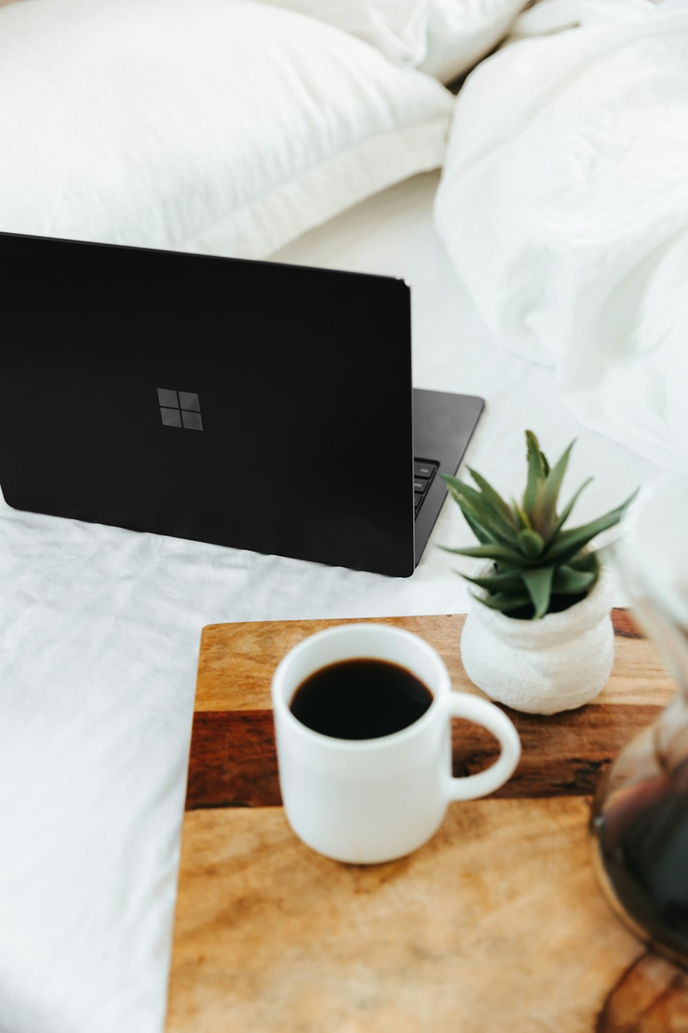 Computadora portátil Microsoft Surface negra junto a una taza de cerámica blanca sobre una cama blanca 