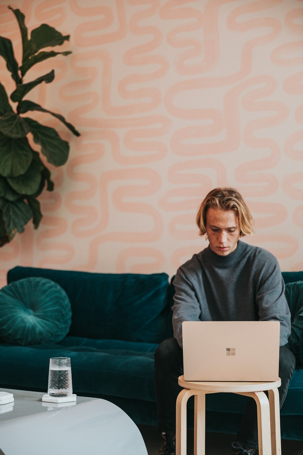 man in gray turtle neck shirt sitting on blue couch using a Microsoft Surface 3 sandstone laptop 