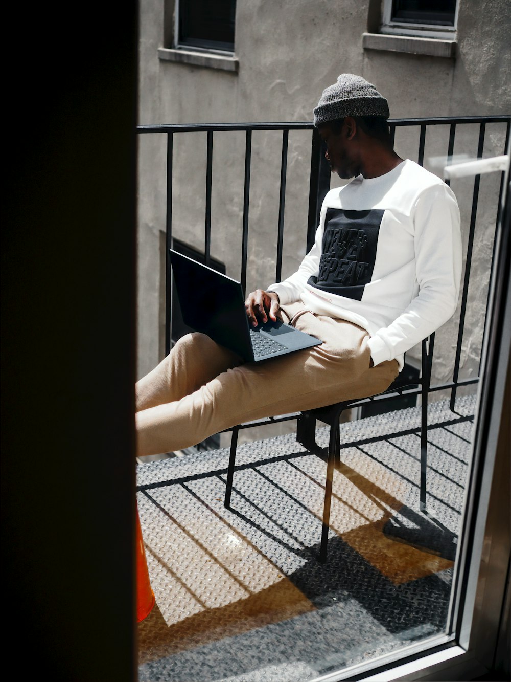 man in white shirt sitting on his balcony working on a cobalt blue microsoft surface laptop 
