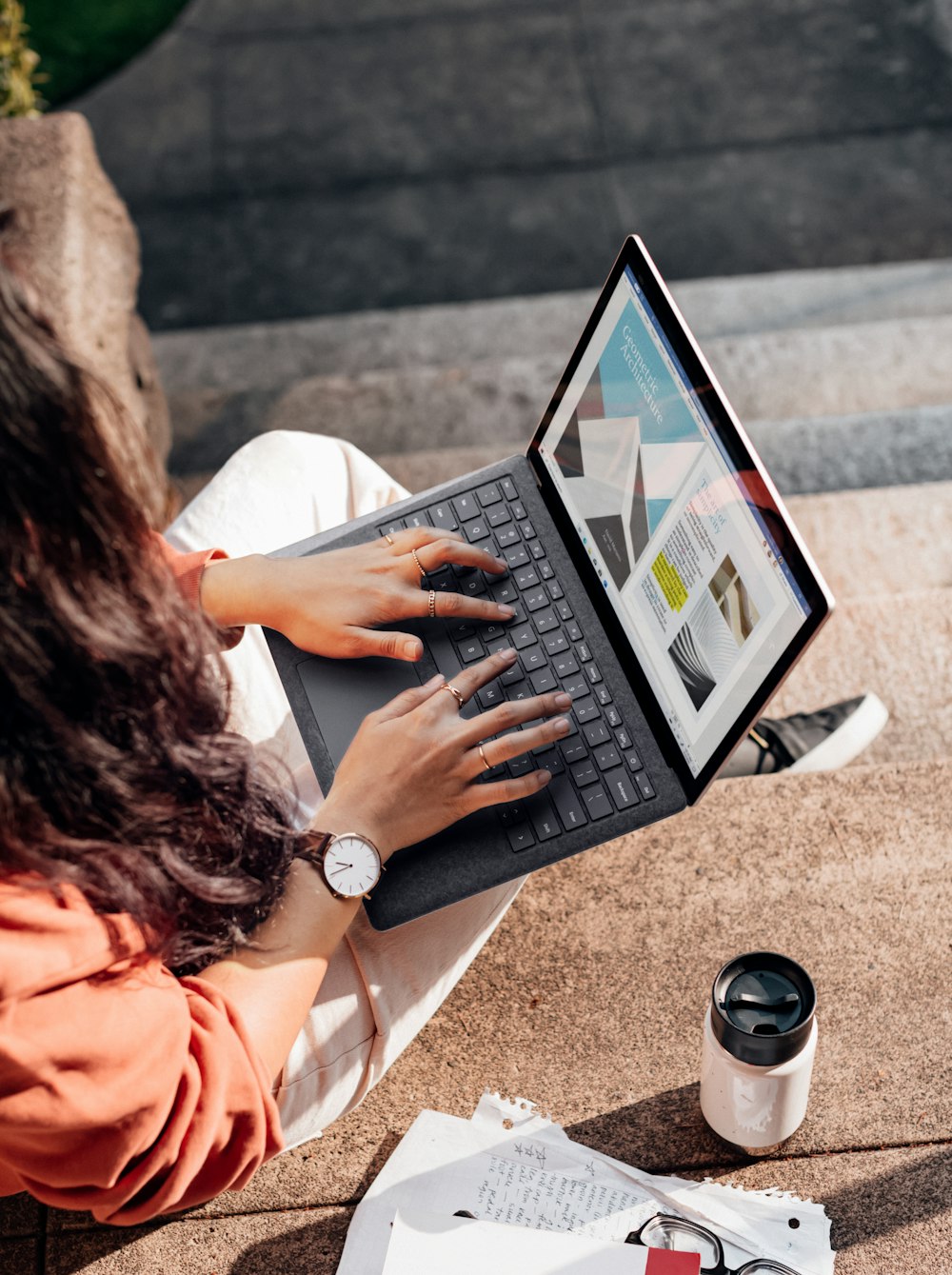 woman in orange long sleeve shirt using silver microsoft surface laptop computer