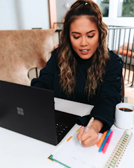 woman in black sweater with a black microsoft surface laptop on a table 