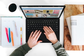 A person using a laptop with stationery and a cup of coffee.