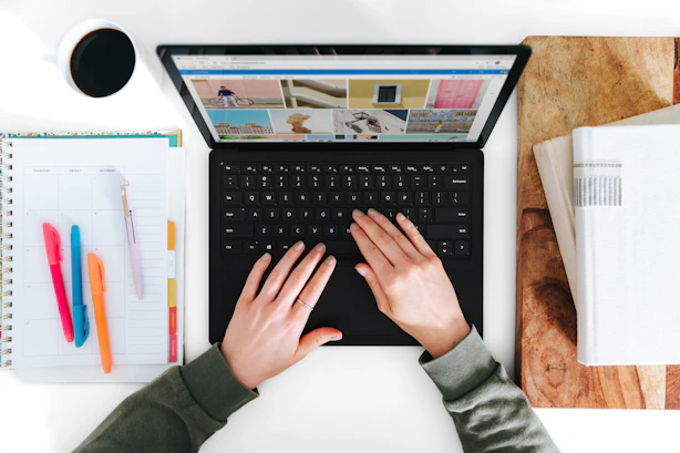 A smiling blogger typing on a laptop with a cup of coffee nearby, surrounded by colorful stationery.