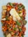 A colorful mix of cut vegetables and tofu is presented on a plate, featuring bright orange carrots, green beans, and red peppers. There is a piece of fried egg on top, adding a contrasting texture and color.