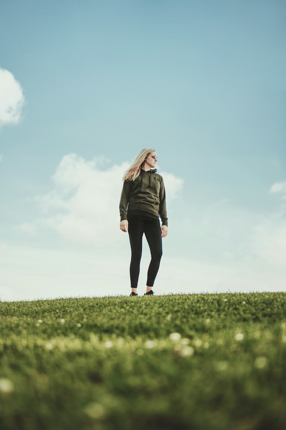 woman in black jacket standing on green grass field under blue sky during daytime
