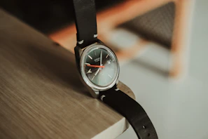 Close-up of a sleek classic watch with a leather strap resting on a dark wooden surface.