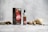 A small bottle labeled 'Spice Drops' placed next to a cardboard box with the same branding, surrounded by an assortment of whole spices, including ginger, nutmeg, and peppercorns, on a textured light gray surface.