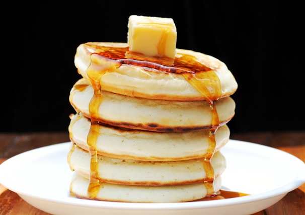 Close-up of fluffy soufflé pancakes stacked high with syrup dripping down.