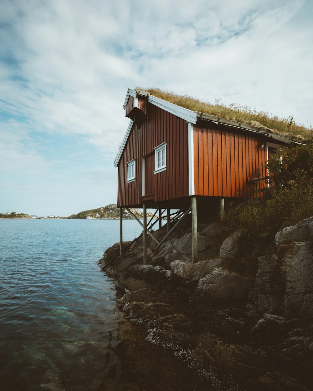 red and white wooden house on brown rock formation near body of water during daytime