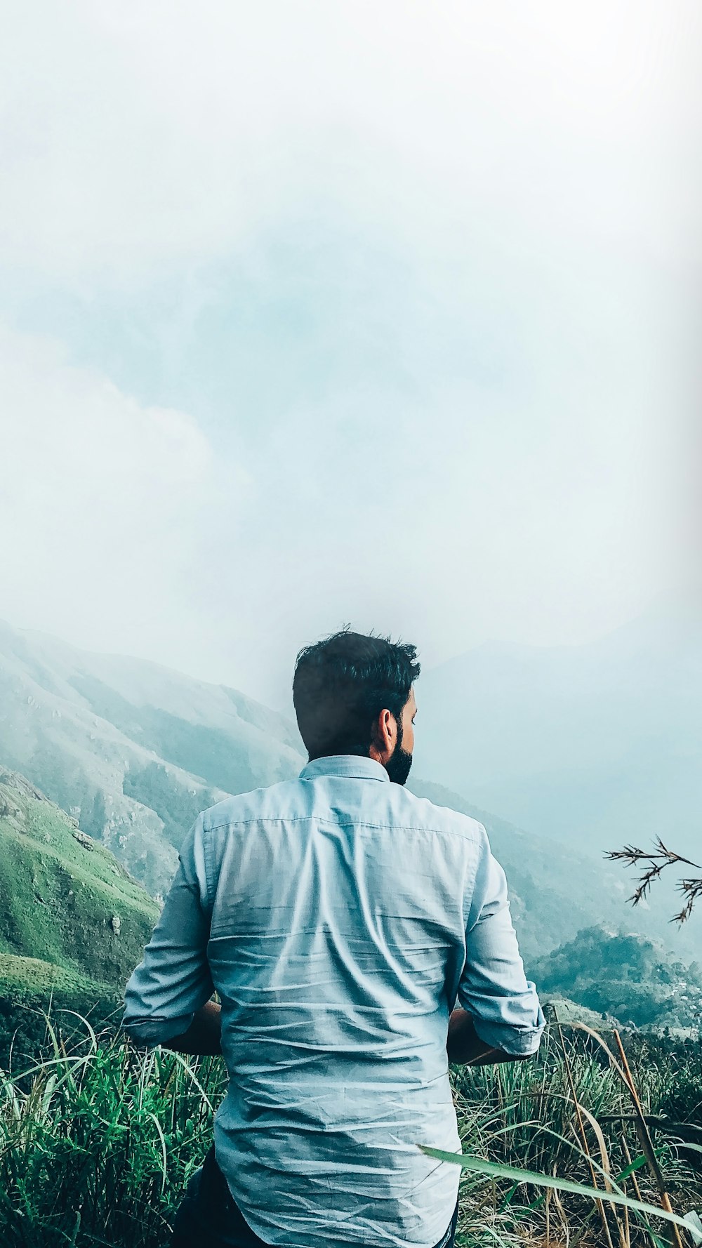 man in blue dress shirt standing on top of mountain during daytime