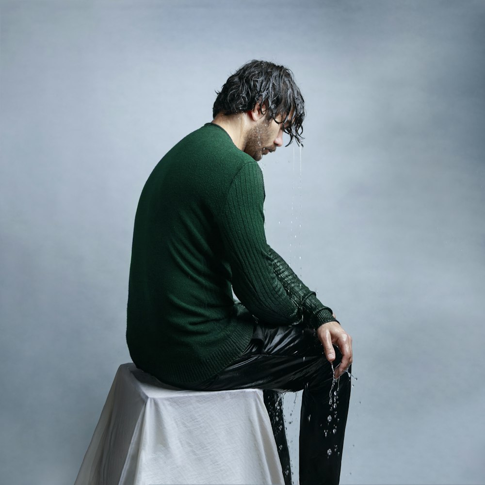 man in green long sleeve shirt and black pants sitting on white chair