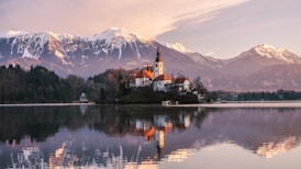 brown and white concrete building near lake and mountain under white clouds during daytime