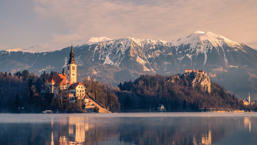 Edificio in cemento marrone e bianco vicino al lago e alla montagna coperta di neve durante il giorno