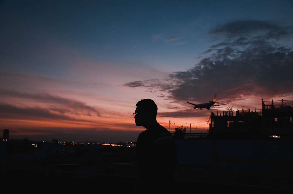 silhouette of man standing near body of water during sunset