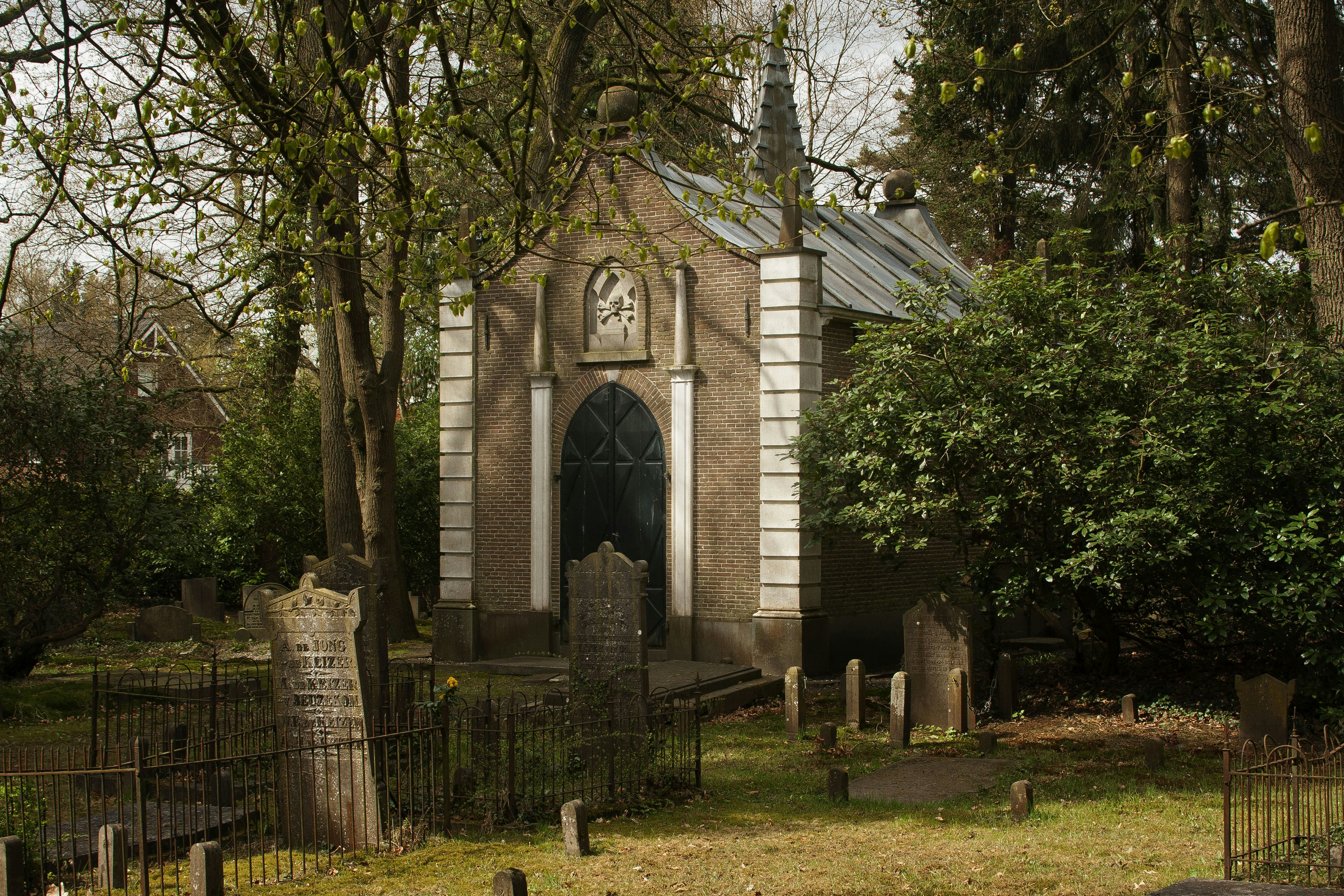 A close-up shot of the weathered stone crosses and tombstones in the old Dutch Cemetery, partly obscured by overgrown foliage, conveying an eerie historical atmosphere.