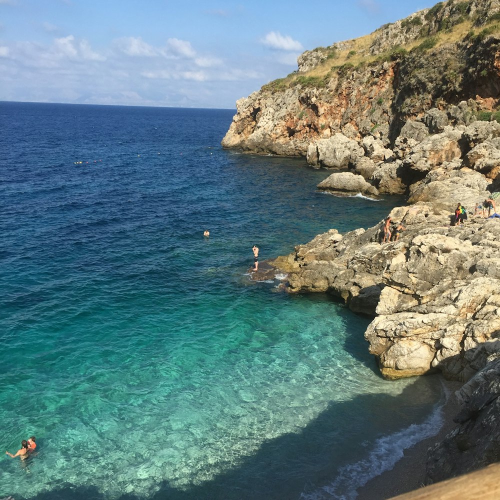 people swimming on sea near rocky mountain during daytime