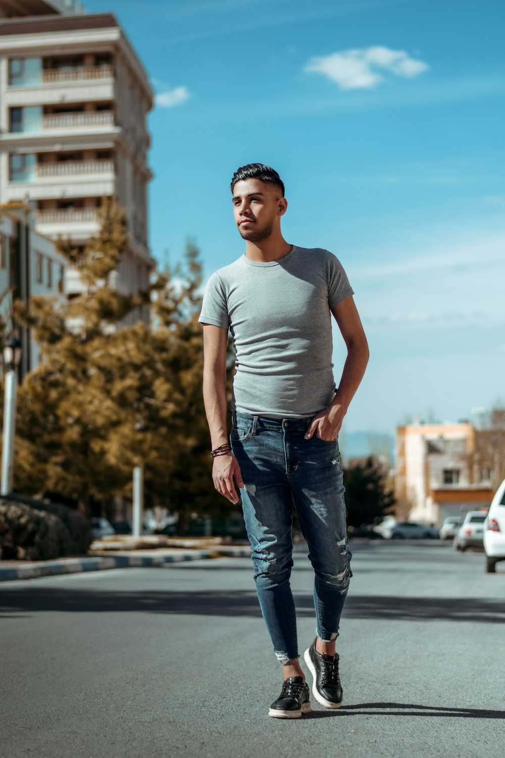 man in white crew neck t-shirt and blue denim jeans standing on road during daytime