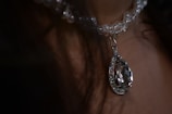 A close-up view of a clear beaded necklace featuring a large pear-shaped crystal pendant with intricate detailing, hanging against a neutral background.