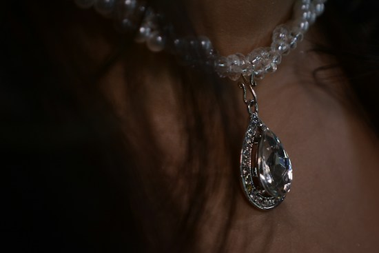 A close-up view of a clear beaded necklace featuring a large pear-shaped crystal pendant with intricate detailing, hanging against a neutral background.