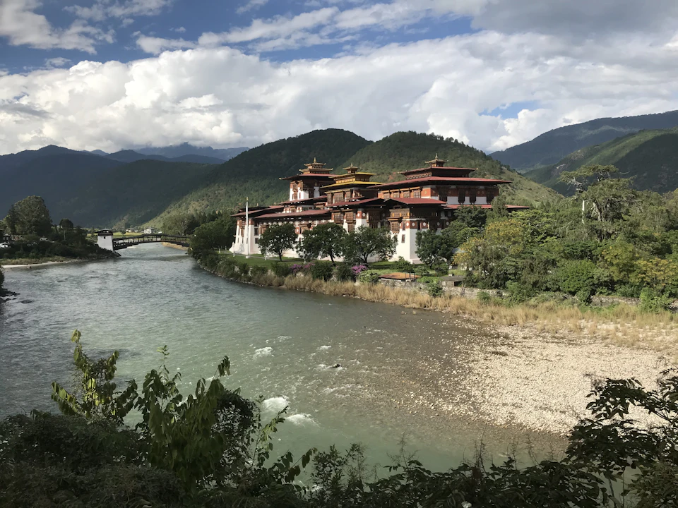 Punakha Dzong on its riverbank below forested hills, the covered cantilever bridge crossing the water at left