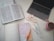 A neatly arranged workspace featuring an open black laptop, an open book with text, a notebook displaying a motivational quote written in neat handwriting, several colored marker pens, a stack of colorful washi tapes, and a pink and cream striped mug filled with a beverage.
