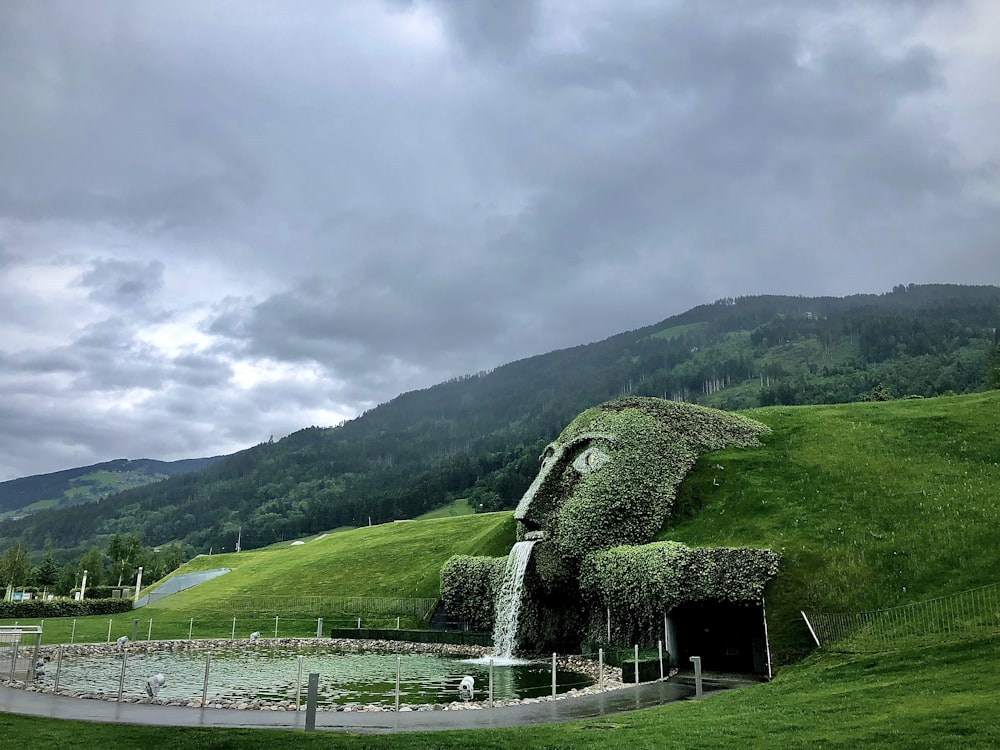 campo de grama verde perto da montanha verde sob nuvens brancas durante o dia