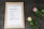 A framed checklist titled 'Publish Blog Post' is displayed on a textured, dark surface. The checklist includes steps such as brainstorming ideas, writing text, taking photos, recording video, setting a publish date, and sharing on social media platforms like Facebook, Twitter, and Pinterest. Next to the frame are two roses, one pink and one white with pink edges, accompanied by green leaves.