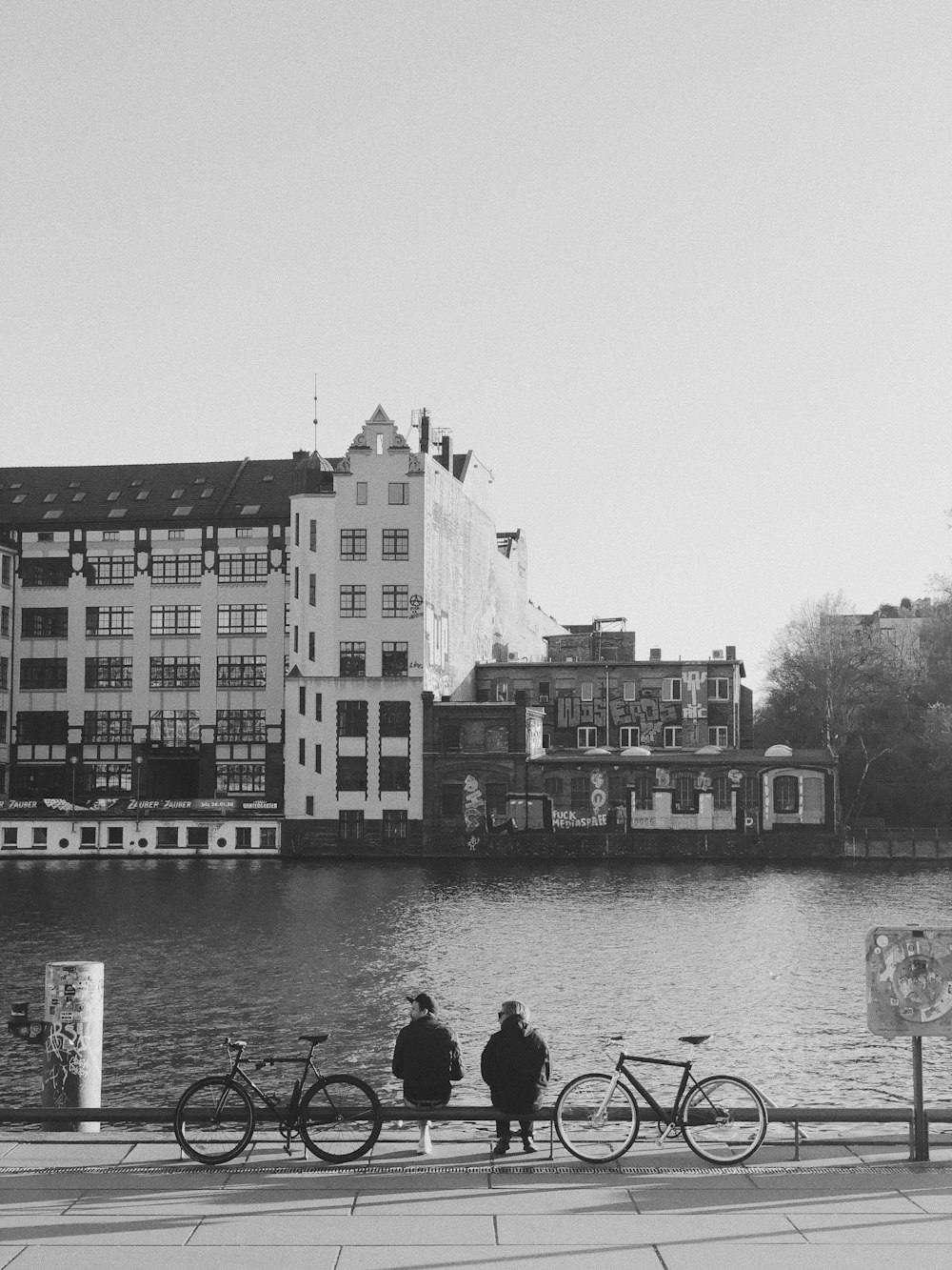 grayscale photo of people walking on sidewalk near body of water and buildings