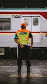 man in orange helmet and green and blue stripe polo shirt standing beside white and red
